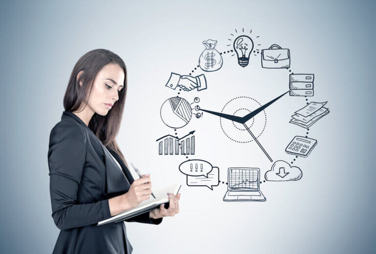Portrait of a beautiful young businesswoman wearing a black suit and holding a planner and a pen taking notes. Gray wall background with a black time management sketch on it.