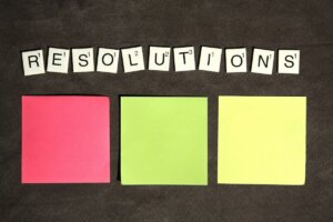 Resolutions in Scrabble tiles above 3 blank post it notes.