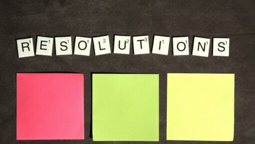 Resolutions in Scrabble tiles above 3 blank post it notes.