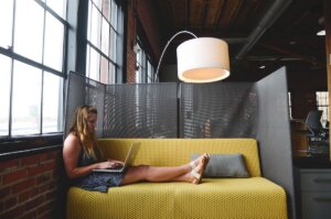 A woman writing on a laptop in a shared coworking space with a couch.