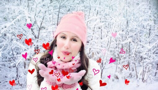 A woman in a snow filled forest blowing hearts for Valentine's Day