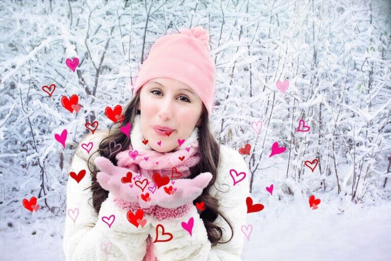 A woman in a snow filled forest blowing hearts for Valentine's Day