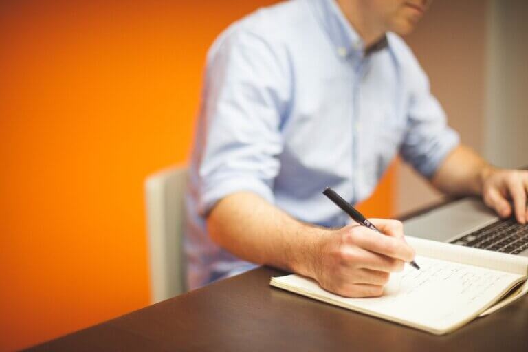 A man sitting in front of a computer with a notepad taking notes.