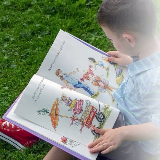 A little boy sitting in the grass reading a children's picture book.